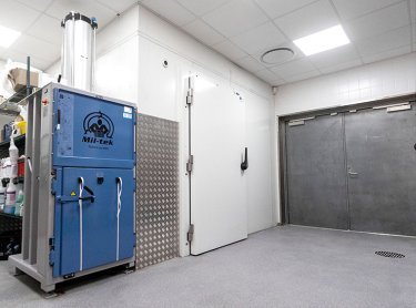 Presse à balles Mil-tek A305 bleue dans une zone de stockage arrière
