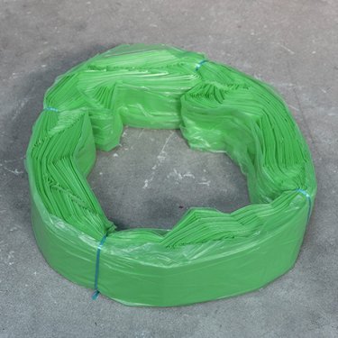 Cartouche de sacs en plastique verts Infinity format XL, liée avec du fil bleu, disposée en anneau sur une surface grise